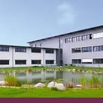 Modernes Gebäude vor einem Teich mit grüner Wiese